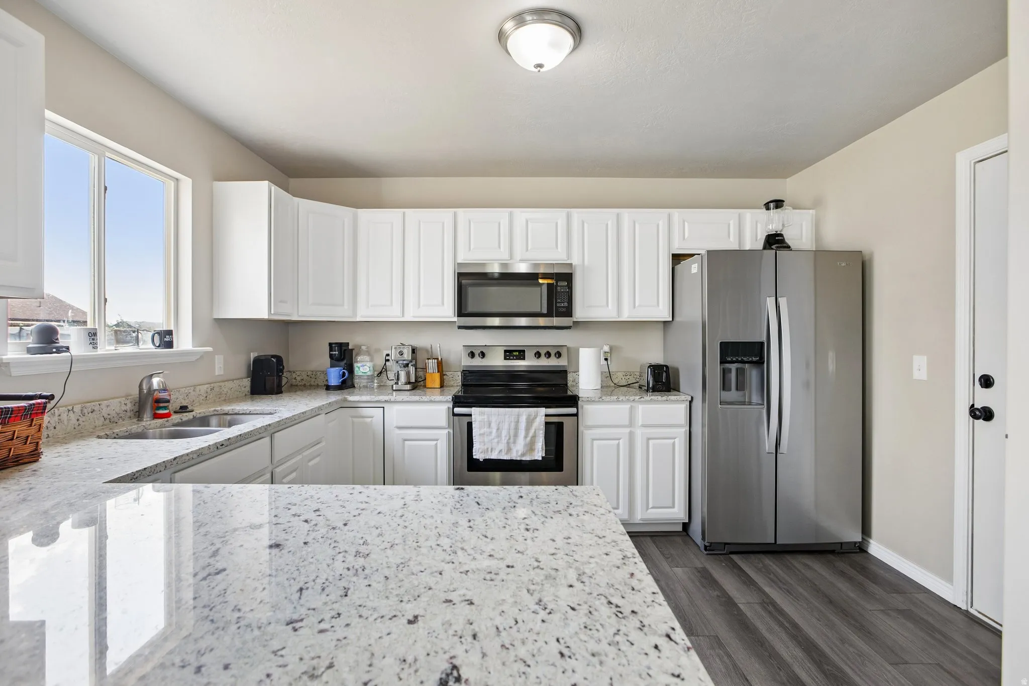 Kitchen featuring white cabinetry, light granite countertops, stainless steel appliances, and dark wood-finish flooring