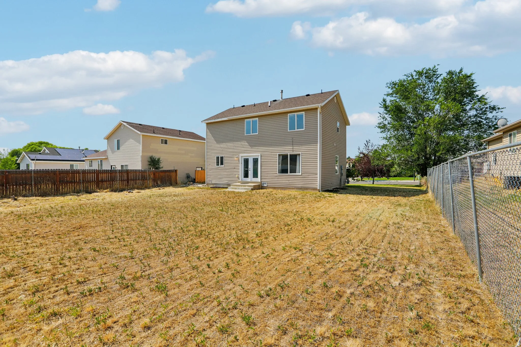 Expansive backyard featuring a two-story residence with light-colored siding and a brown roof