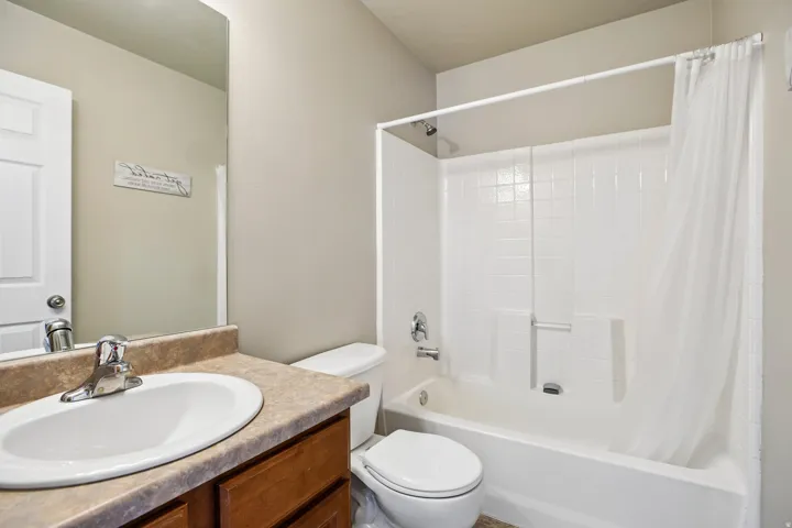 Bathroom featuring a white vanity sink, a brown wood-finish vanity cabinet, a tan countertop, and a shower/tub combination with white subway tile surround