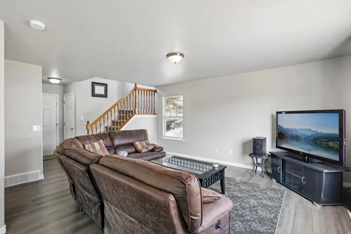 Open-concept living area featuring wood-finish flooring, a light gray color palette, and a prominent staircase with natural wood railings
