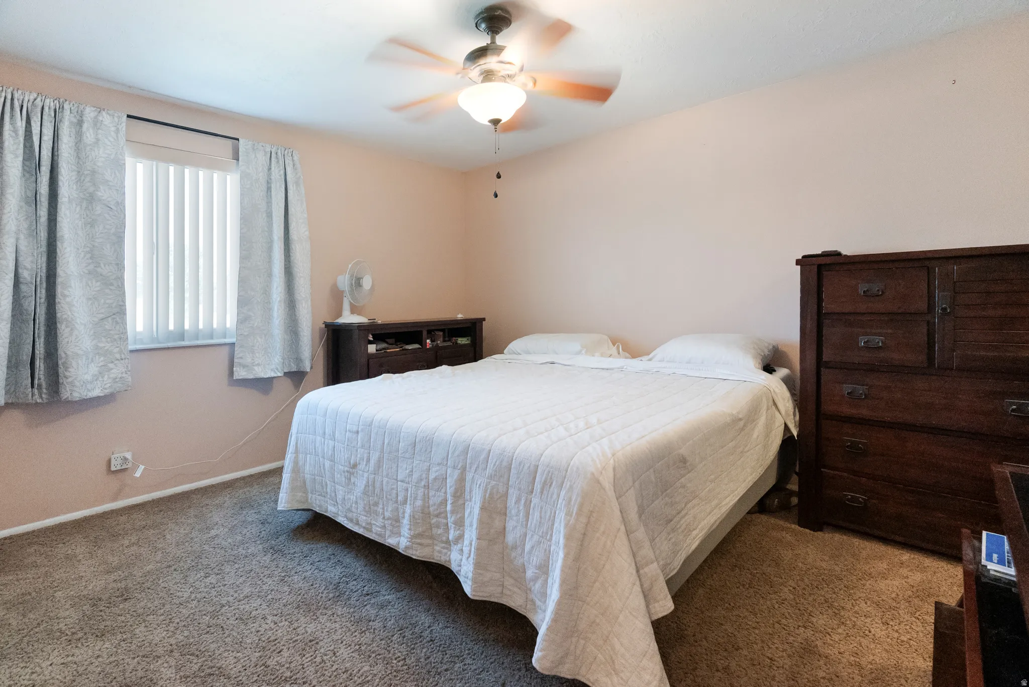 Carpeted room featuring a ceiling fan with integrated lighting, a window with vertical blinds, and neutral wall tones