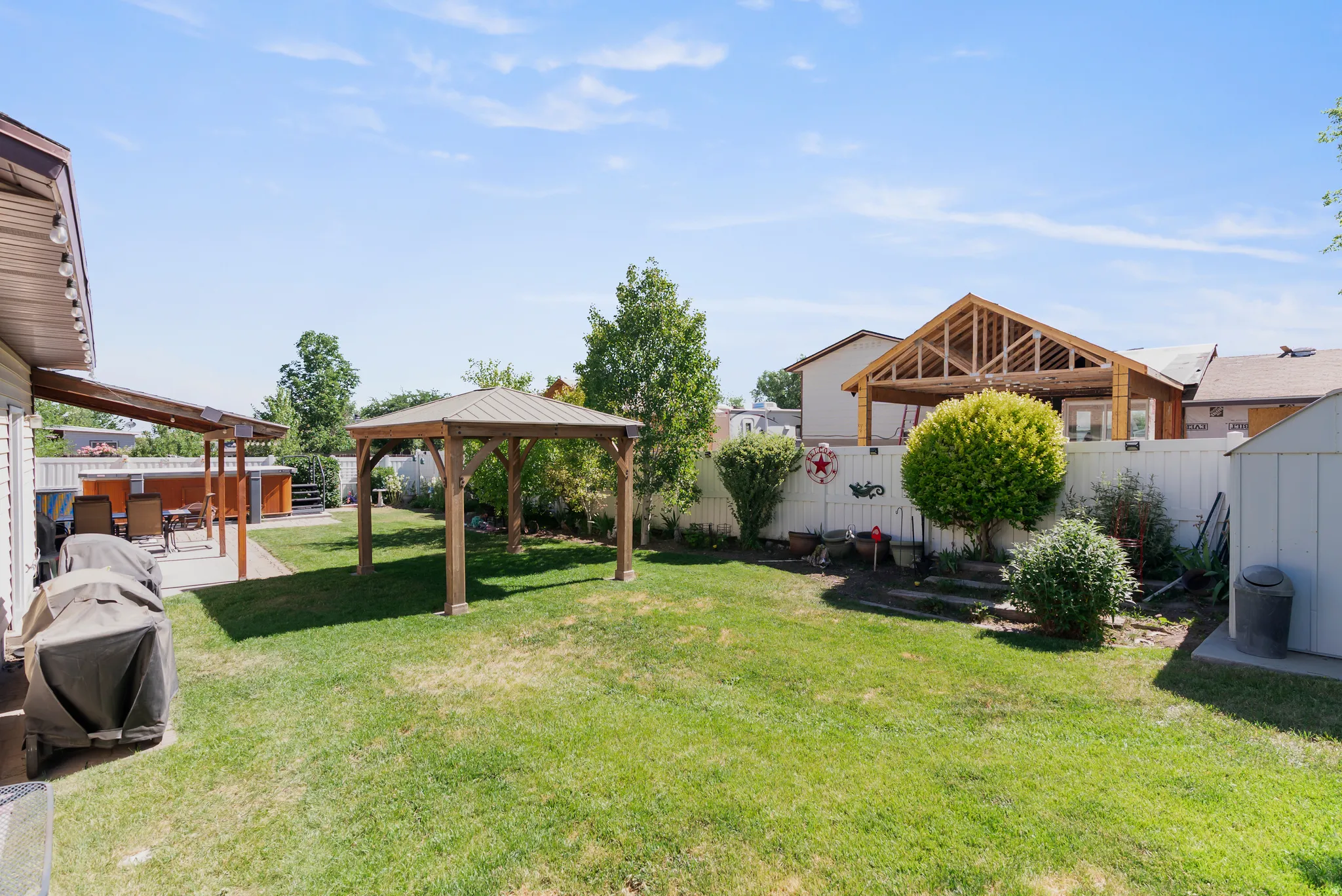 Expansive backyard featuring a central wooden gazebo with a metal roof, a covered patio area, and a white privacy fence