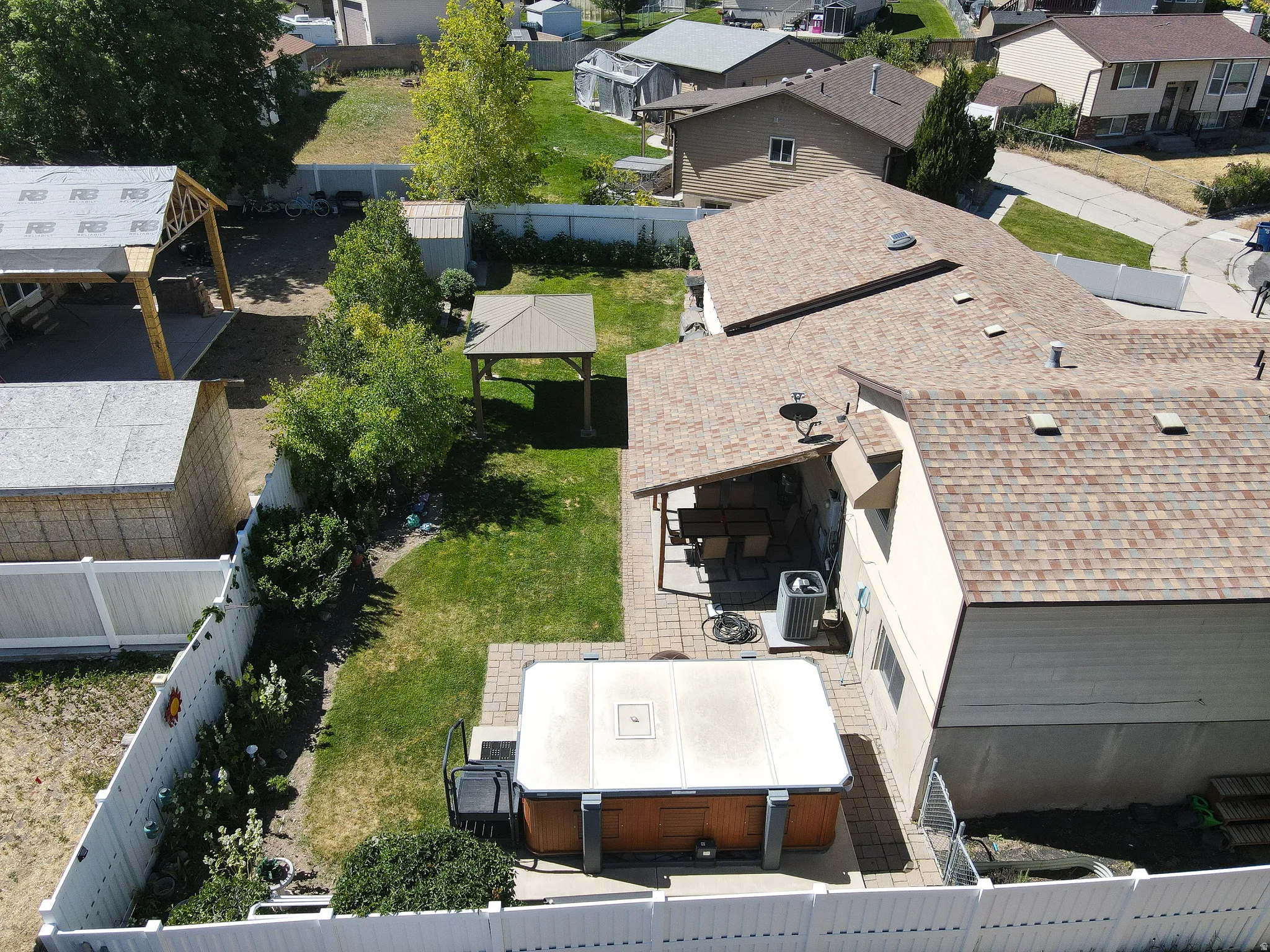 Expansive backyard featuring a hot tub on a paver patio, a covered patio area, and a separate gazebo