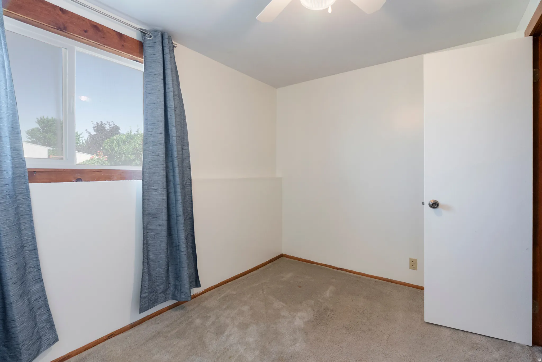 Carpeted room featuring a white ceiling and walls, a window with natural light, and a ceiling fan