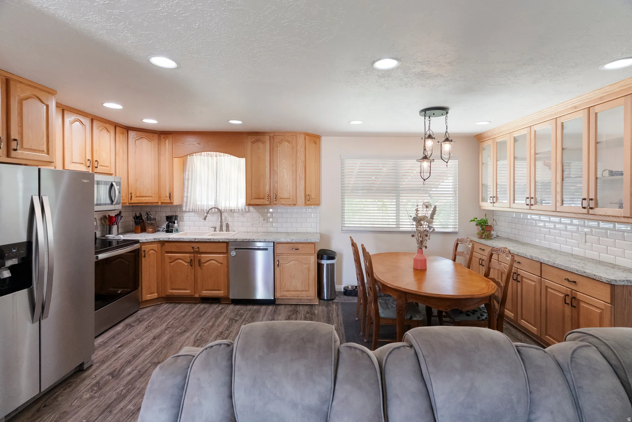 Spacious kitchen and dining area featuring wood cabinetry, stainless steel appliances, granite-style countertops, white subway tile backsplash, and wood-finish flooring