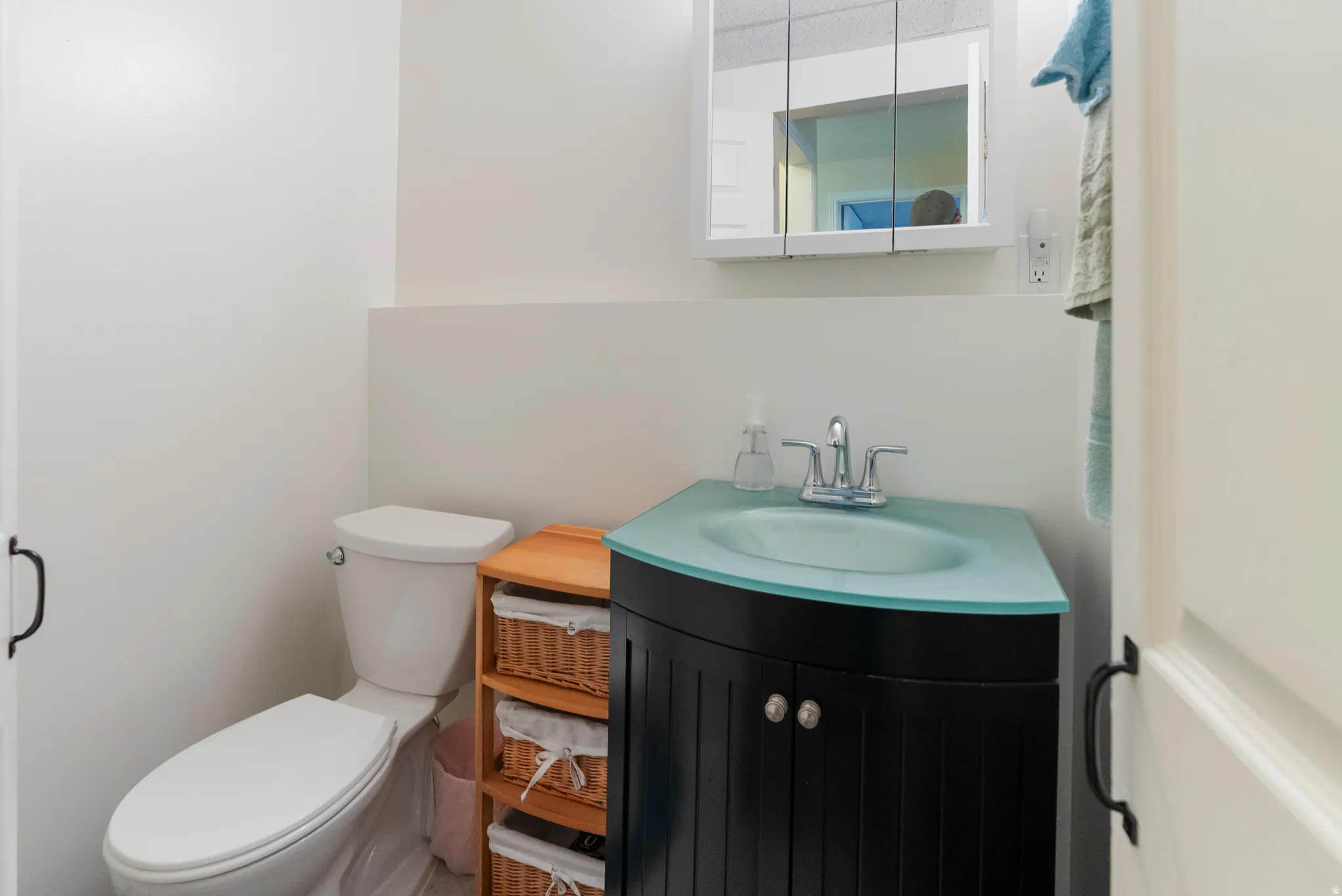 Bathroom featuring a white toilet, corner vanity with a light blue countertop and integrated sink, chrome faucet, and mirrored medicine cabinet