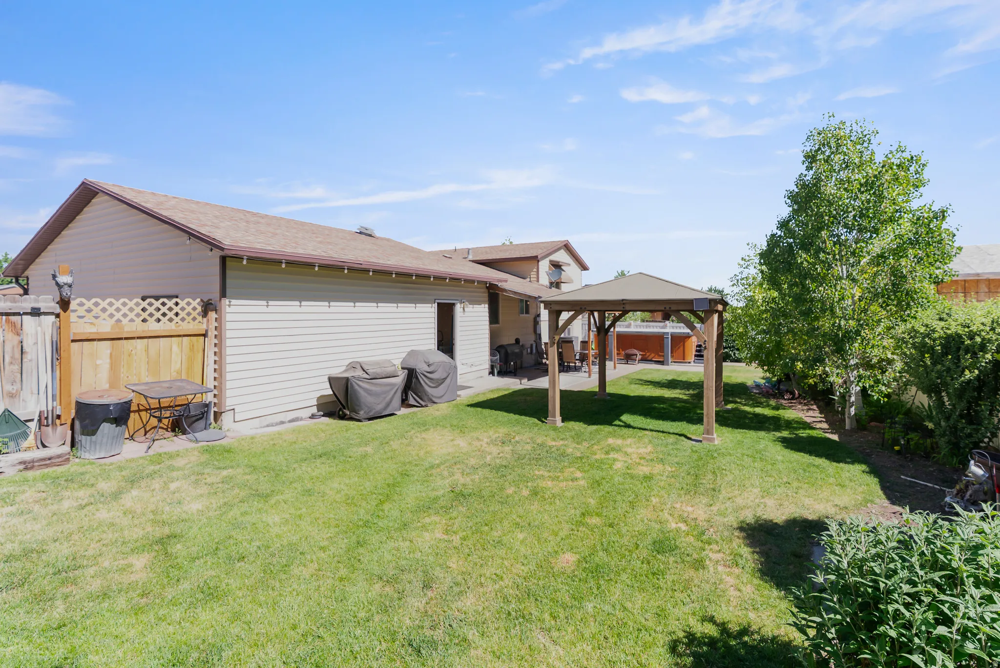 Expansive backyard featuring a large grassy area, a wooden gazebo, and mature trees providing natural shade