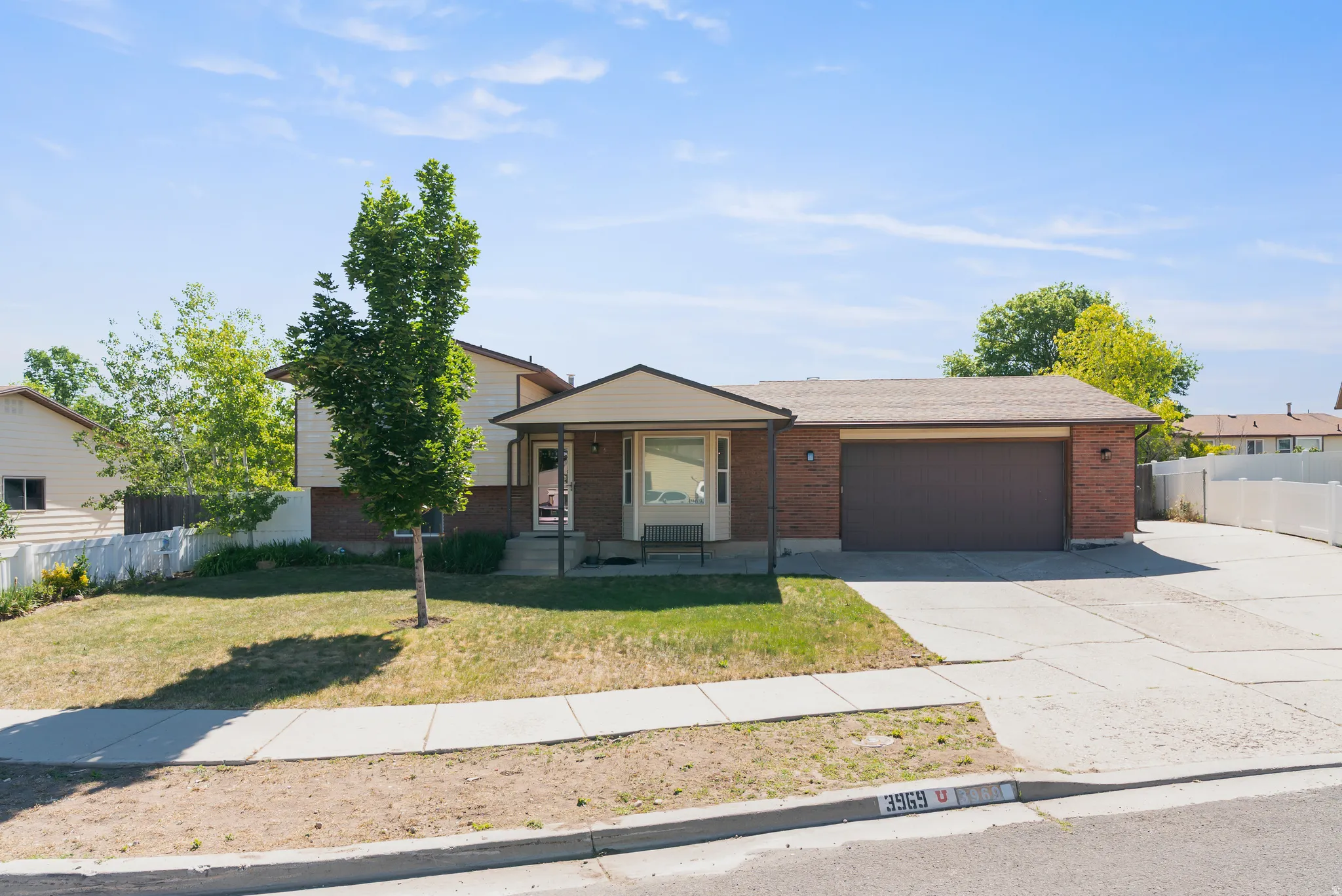 Split-level residence featuring a brick facade, covered entry, attached garage with a concrete driveway, and a front lawn