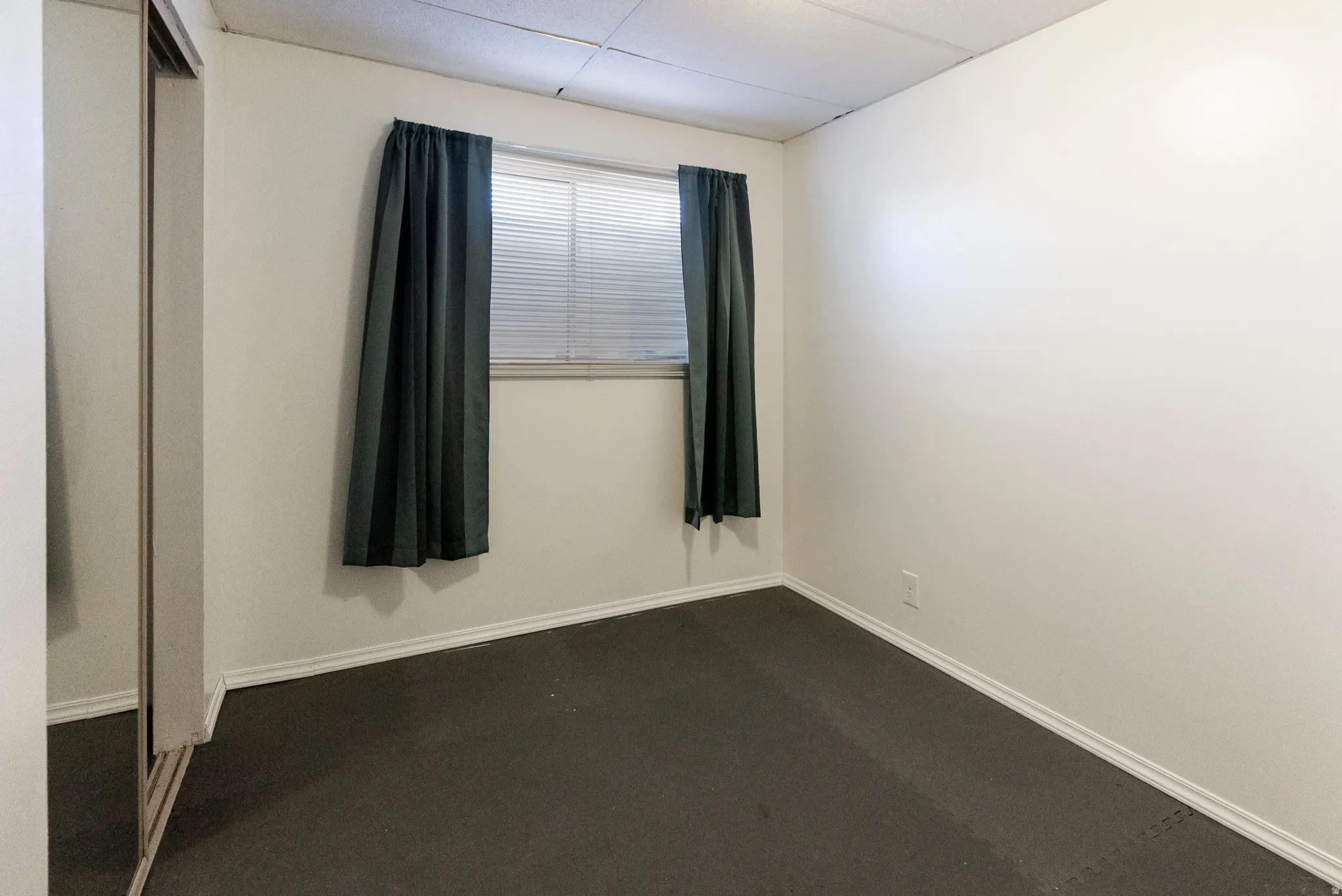 Interior room featuring a window with blinds, white walls, and a dropped ceiling