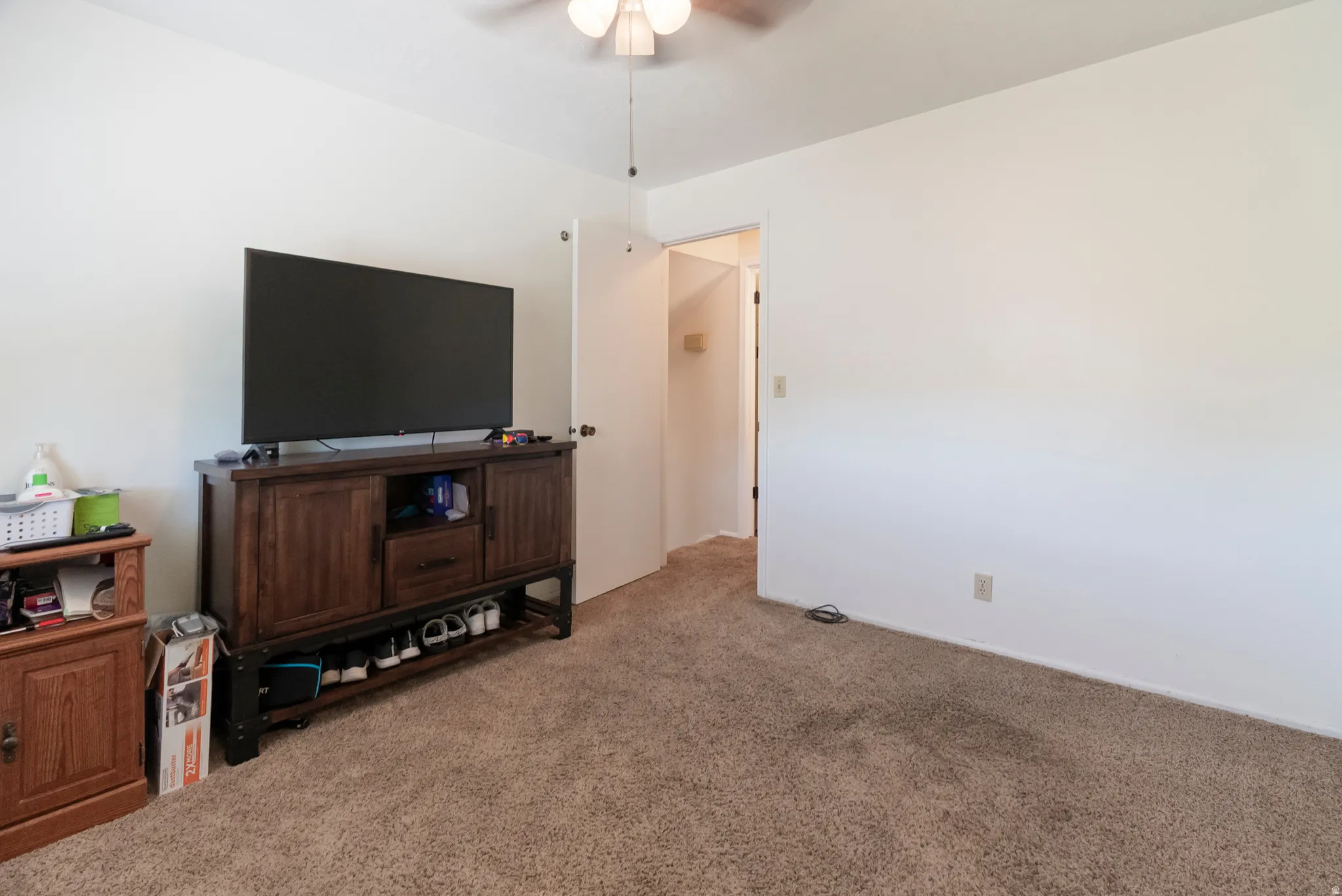 Neutral-toned wall paint and carpeting in a room featuring a ceiling fan with integrated lighting, a closed white door, and a partially open doorway