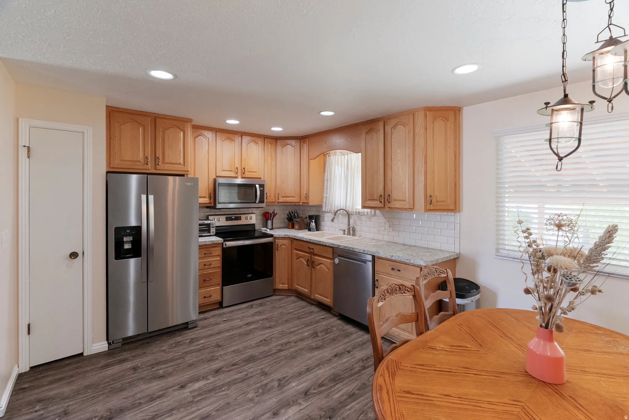 Kitchen featuring wood cabinetry, stainless steel appliances, white subway tile backsplash, and light-toned countertops