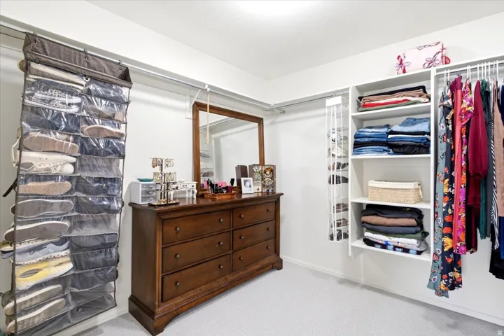 Spacious walk-in closet featuring white wall-mounted shelving and ample hanging rod space