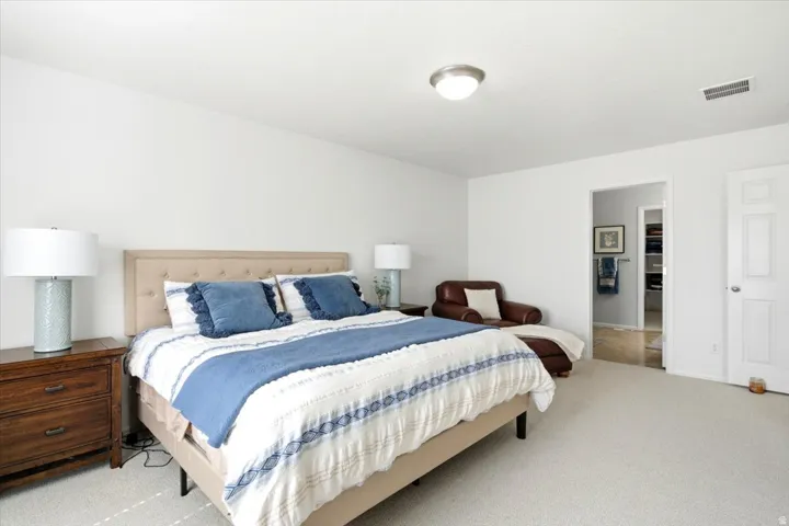 Bright bedroom with neutral wall paint, light-colored carpet flooring, a flush-mount ceiling light fixture, and a paneled white door