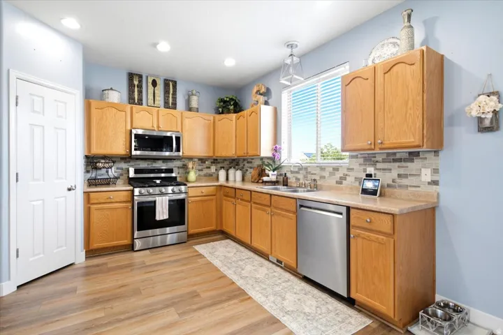 Kitchen featuring wood-finish flooring, light wood cabinetry, a mosaic tile backsplash, and stainless-steel appliances including a range, microwave, and dishwasher