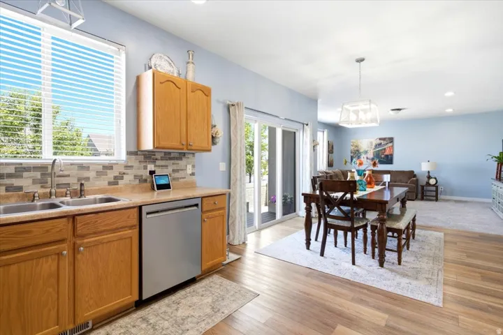 Open-concept living space featuring wood-finish flooring, a kitchen with light wood cabinetry, a stainless steel dishwasher, and a mosaic tile backsplash