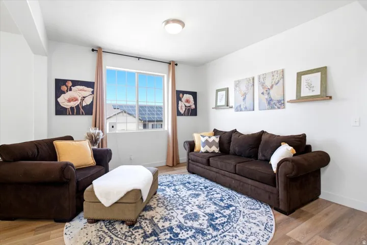 Bright living area featuring wood-finish flooring, a large window with white gridding, white walls, and a ceiling-mounted light fixture