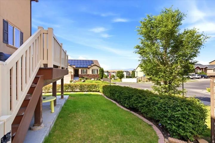 Elevated deck with stairs leading to a grassy yard bordered by a low brick edge and green shrubbery