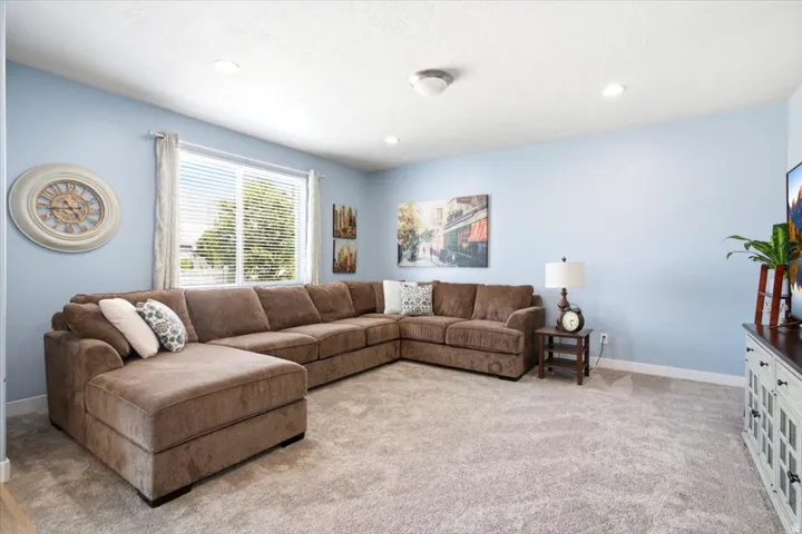 Carpeted living area featuring light blue walls, a large window with blinds, recessed lighting, and white baseboards