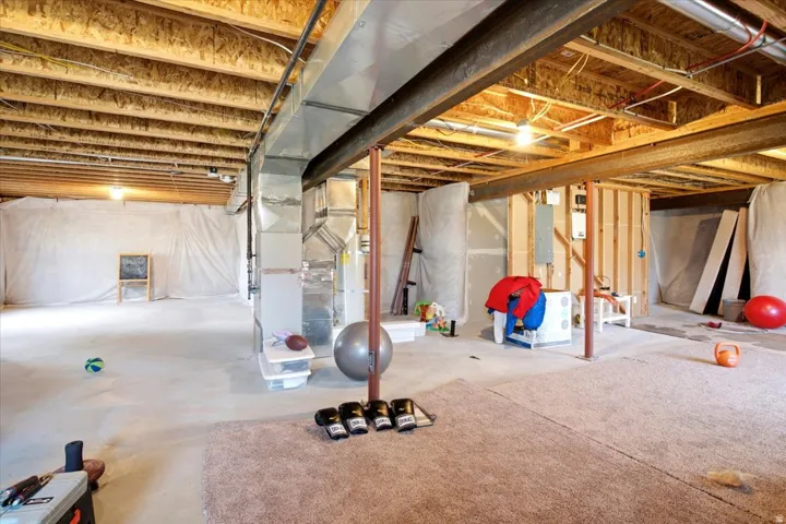 Expansive unfinished basement featuring exposed ceiling joists, substantial steel I-beams, extensive ductwork, a partial carpeted area, and a concrete floor