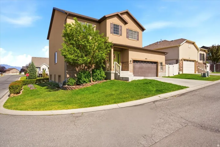 Two-story stucco residence featuring an attached garage, a front porch with railing, and mature landscaping