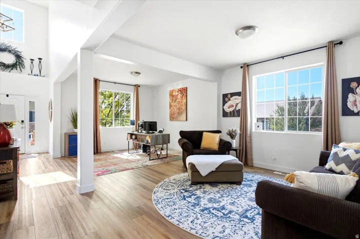 Open-concept living area featuring wood-finish flooring, abundant natural light from large windows, and a high-ceiling entry