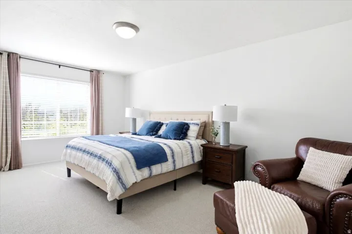 Spacious room featuring light-colored carpet flooring, a large window with horizontal blinds, and a flush-mount ceiling light fixture