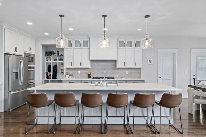Kitchen with light stone countertops, white cabinets, pendant lighting, stainless steel appliances.