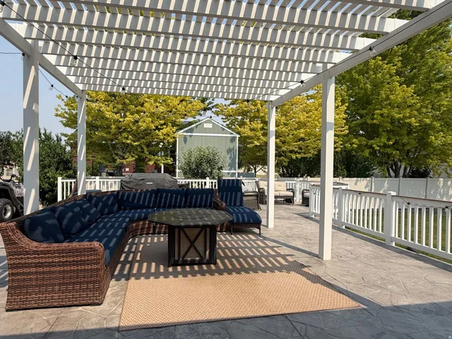 Expansive stamped concrete patio featuring a large white pergola and three sitting areas for entertaining.