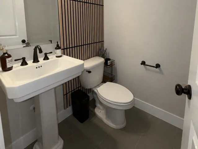 Aesthetic powder room featuring a pedestal sink with a matte black faucet, contemporary wall-mounted lighting, and a slatted accent wall.
