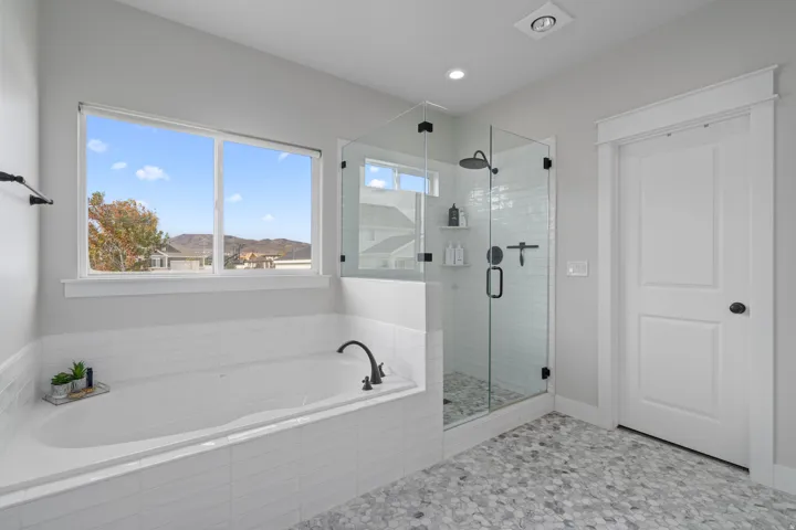 Master Bathroom featuring a spacious soaking tub with dark bronze fixtures, a glass-enclosed shower with subway tile surround and dark bronze fixtures, and a dual-pane window