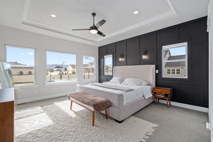 Master room featuring a tray ceiling with recessed lighting, an integrated ceiling fan, and a striking black accent wall with decorative paneling.