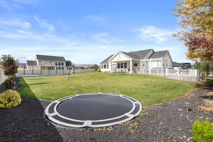 Expansive backyard featuring landscaping with decorative rock, a privacy fence, and a white pergola-covered patio area.
