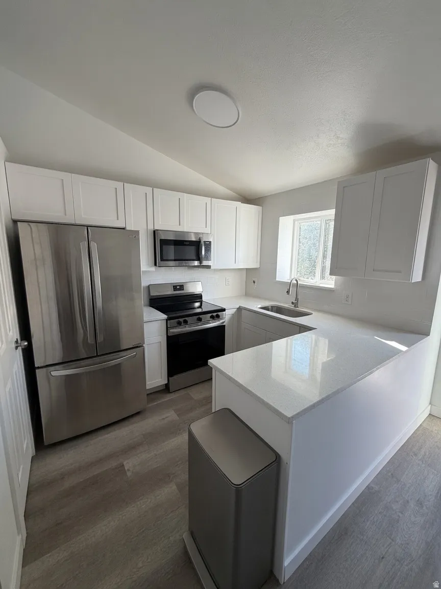 Modern kitchen featuring white cabinetry, light-toned wood-finish flooring, stainless steel appliances, white countertops, and a single basin sink