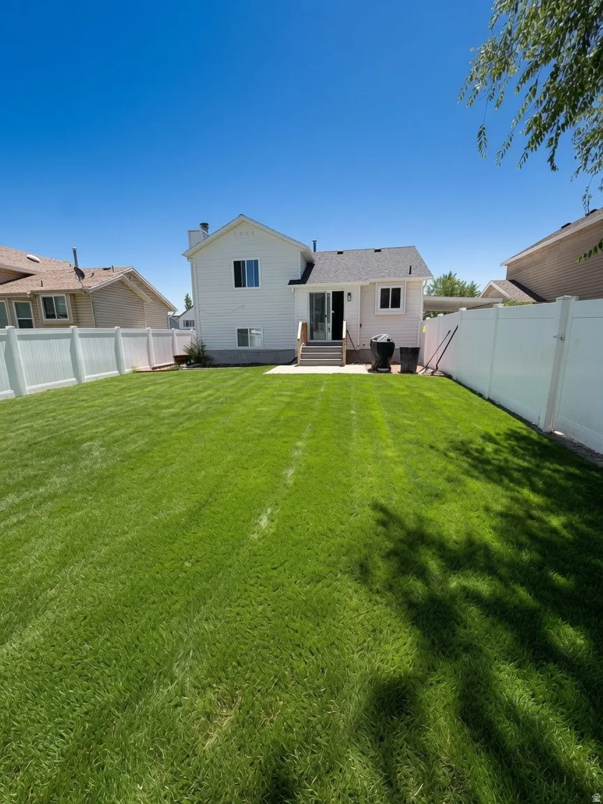 Expansive backyard featuring a manicured lawn, full vinyl privacy fencing, a concrete patio, and exterior access to the residence