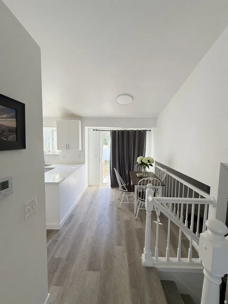 Open-concept main level featuring wood-finish flooring, a white kitchen island with a light-toned countertop, a sliding glass door with dark drapes, and a white staircase with a traditional banister
