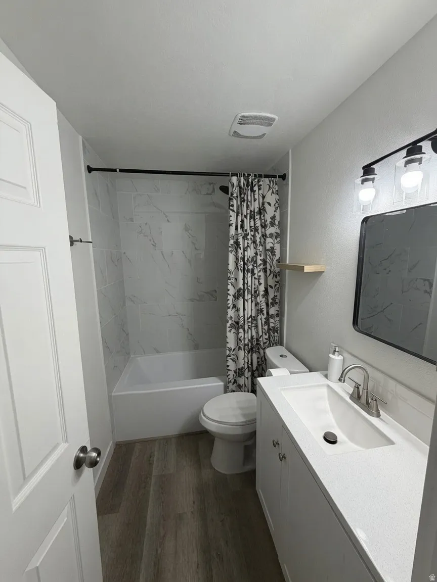 Bathroom featuring a white bathtub with marble-look tile surround, a white vanity with an integrated sink, a dark framed mirror, and wood-finish flooring