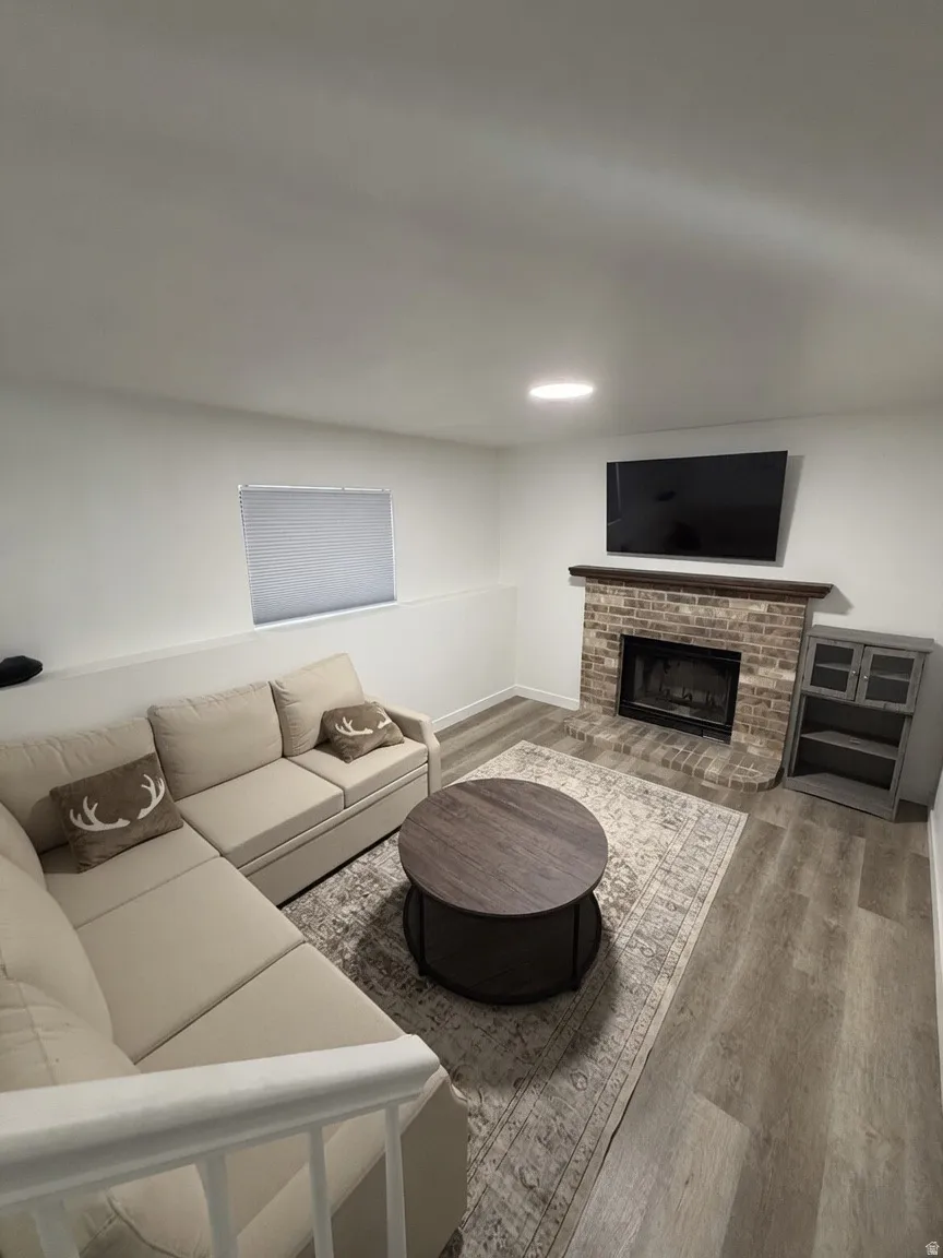 Living area featuring wood-finish flooring, a brick fireplace with a wood mantel, and recessed lighting