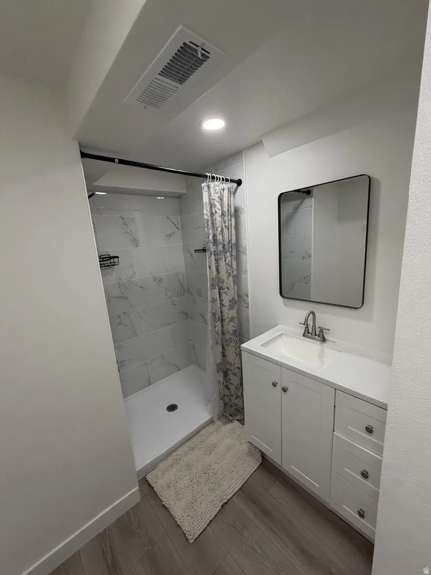 Bathroom featuring a white vanity with an integrated sink, framed mirror, and wood-finish flooring