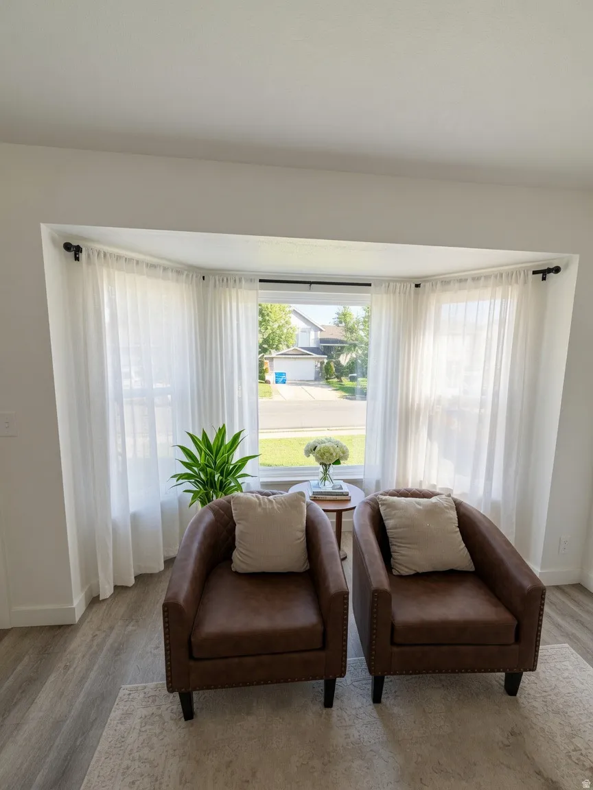Bright bay window with white sheer curtains, light wood-finish flooring, and crisp white baseboards
