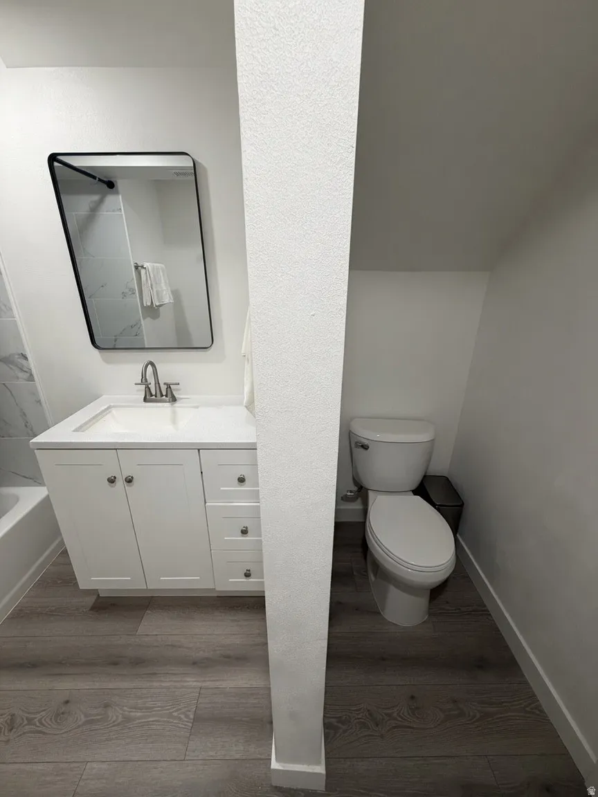 Bathroom featuring a white vanity with integrated sink, rectangular black-framed mirror, wood-finish flooring, and a shower/tub combination with tiled surround