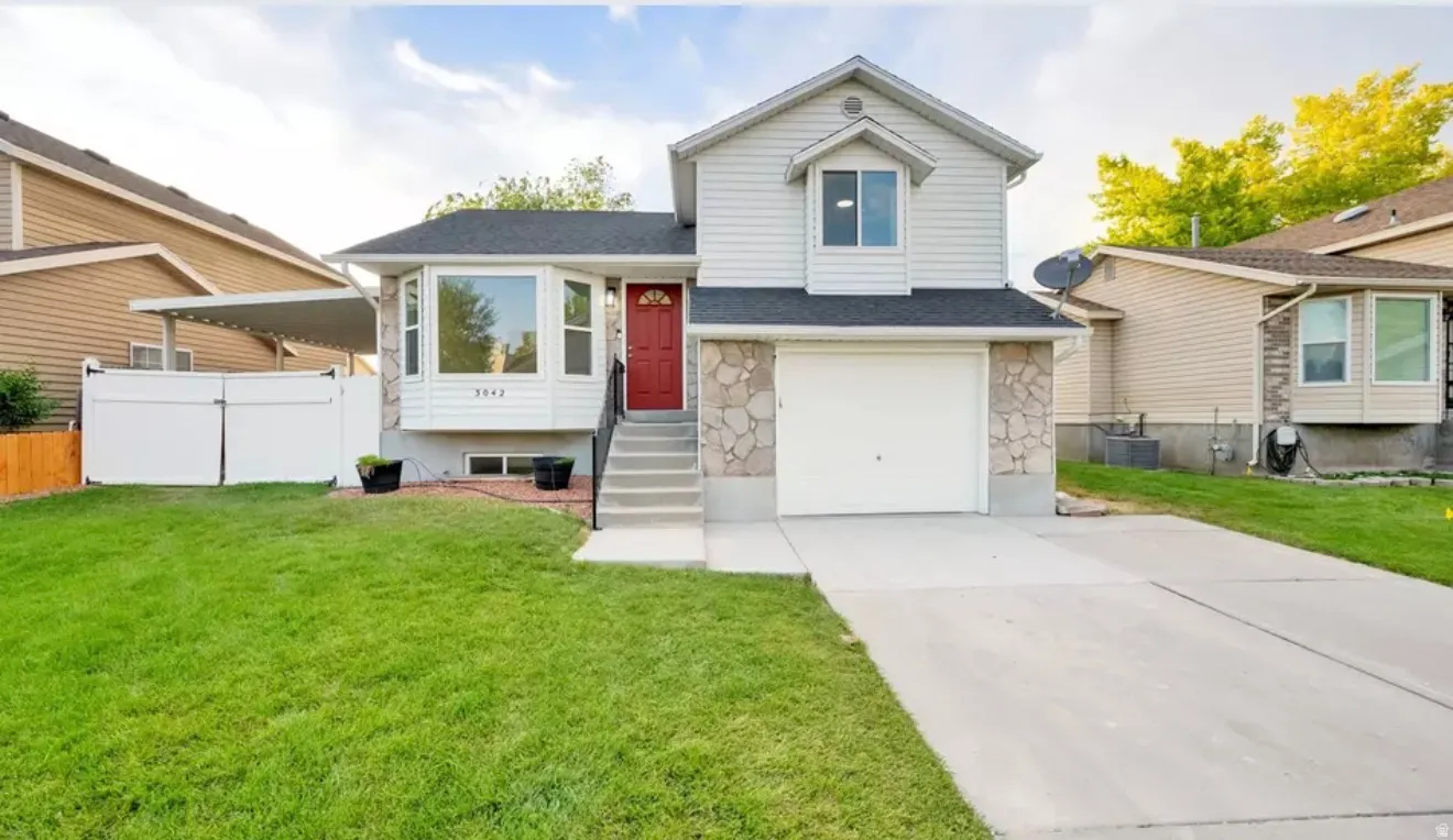 Split-level residence featuring a two-car driveway, attached garage, and a red entry door