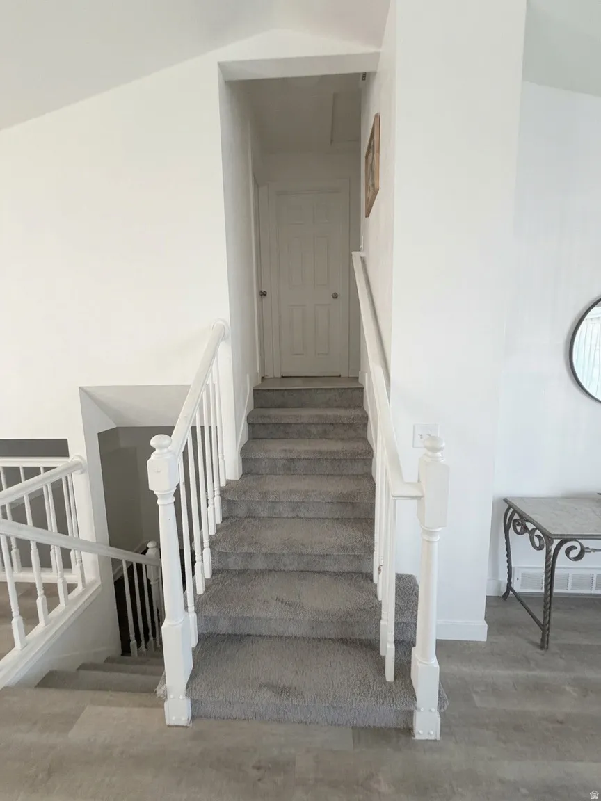 Split-level staircase featuring gray carpeted treads and risers, white painted balusters, and wood-finish flooring at the base