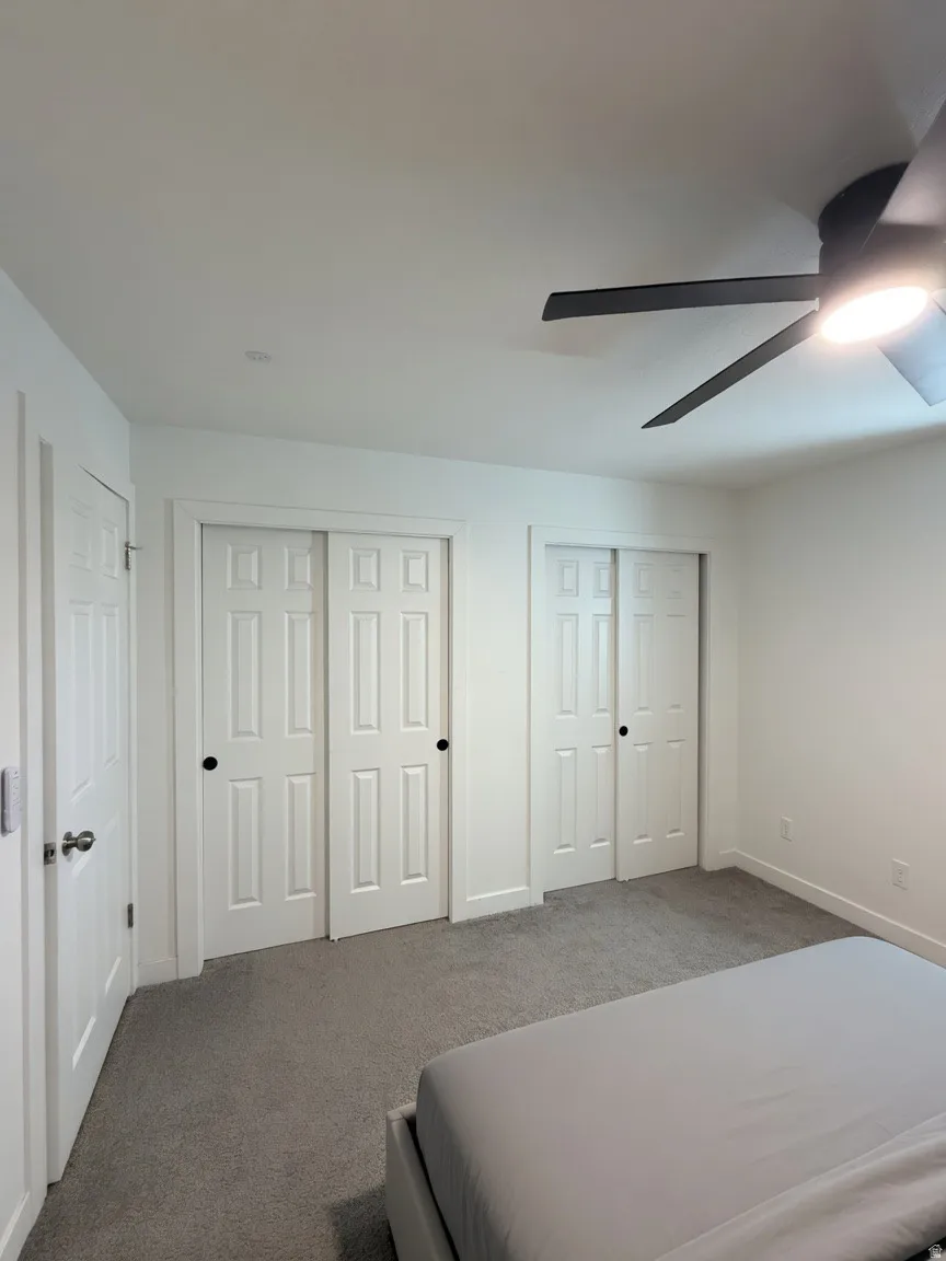 Bedroom featuring two sets of paneled bifold doors, neutral grey carpeting, a modern ceiling fan with integrated lighting, and white baseboards