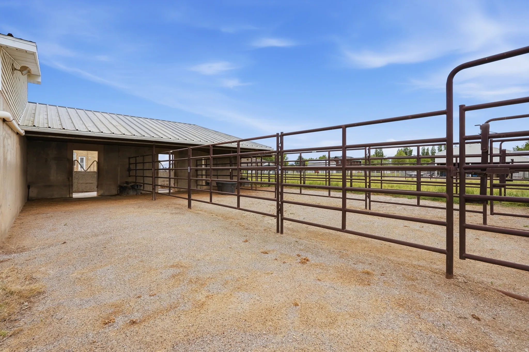 Gravel-surfaced outdoor enclosure featuring brown metal fencing and an adjacent covered structure with a metal roof