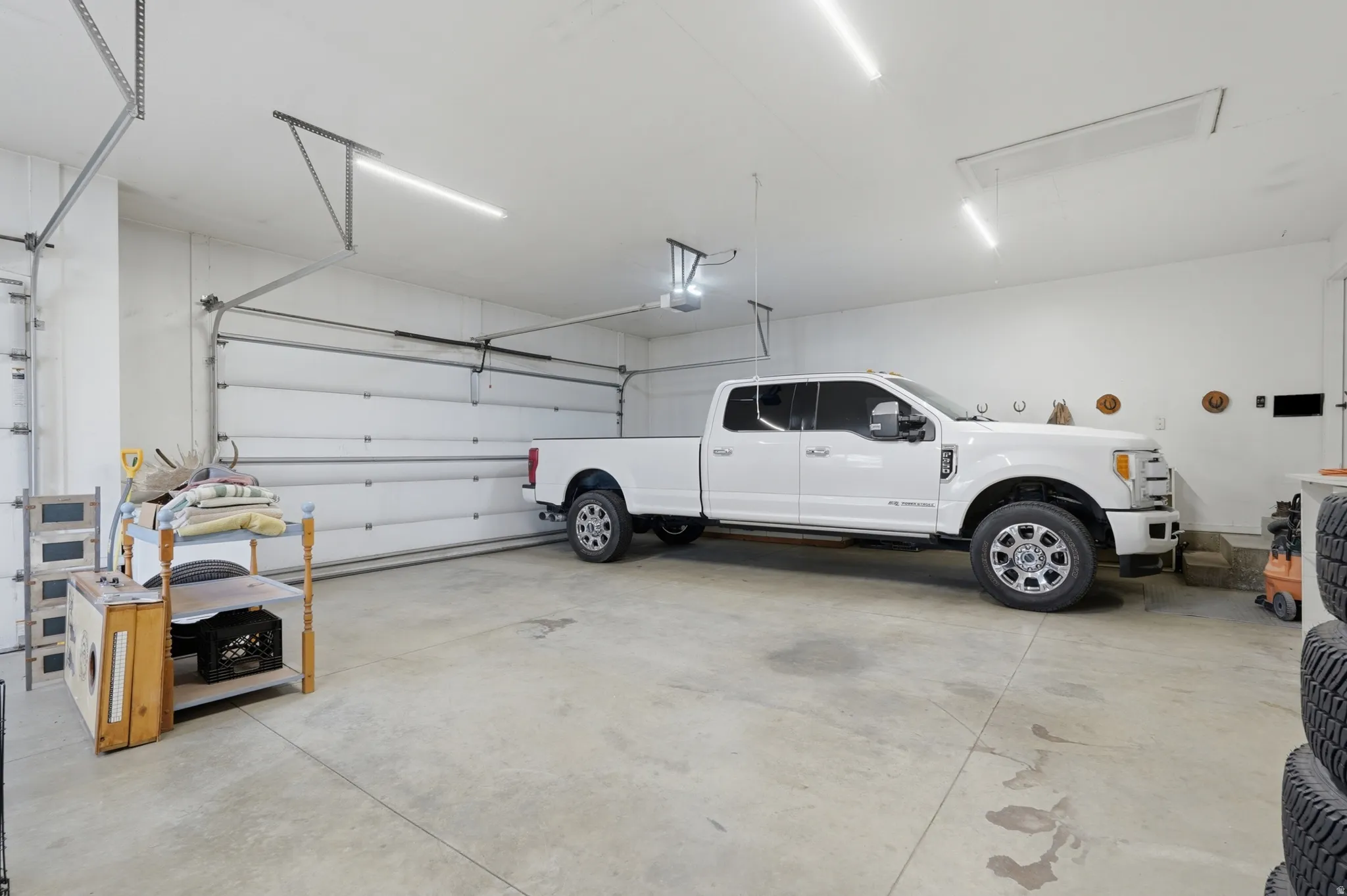 Spacious garage featuring concrete flooring, multiple overhead linear light fixtures, and two overhead garage doors
