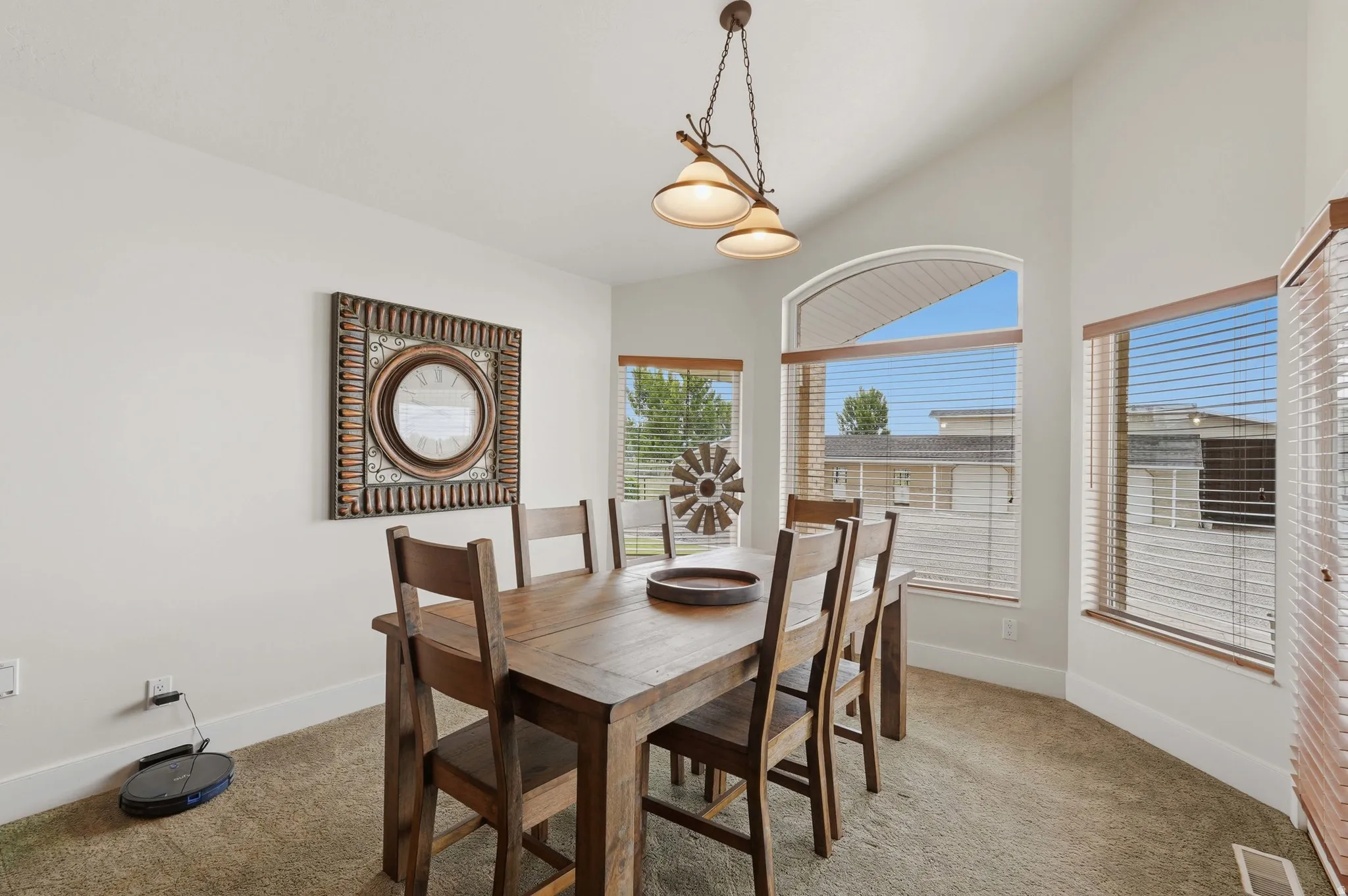 Vaulted ceiling dining area featuring an arched window, multiple windows with blinds, a bronze-finish chandelier, and neutral wall tones