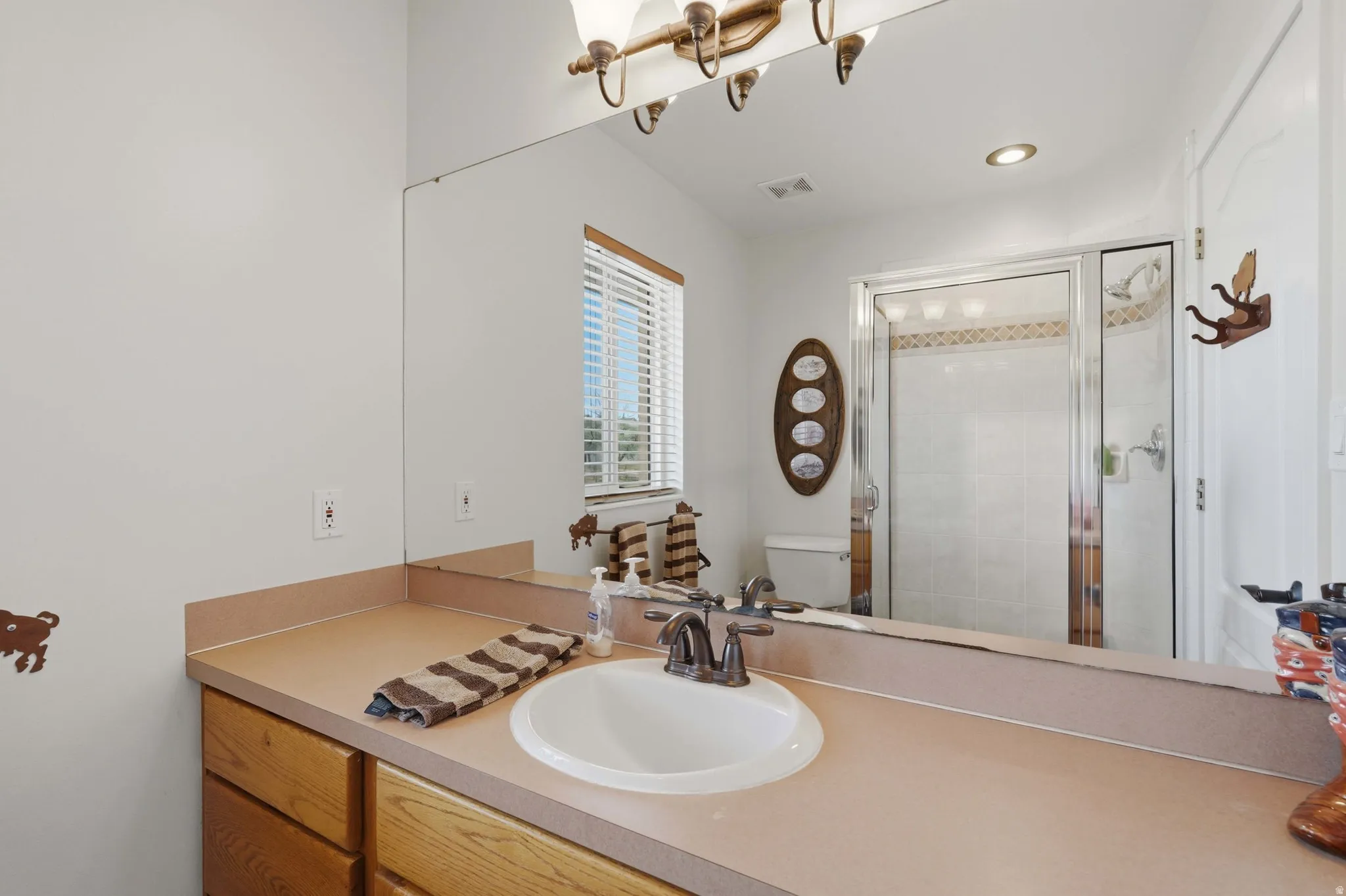 Bathroom featuring a single vanity with an integrated sink, wood-finish cabinetry, a large mirror, and a window with blinds