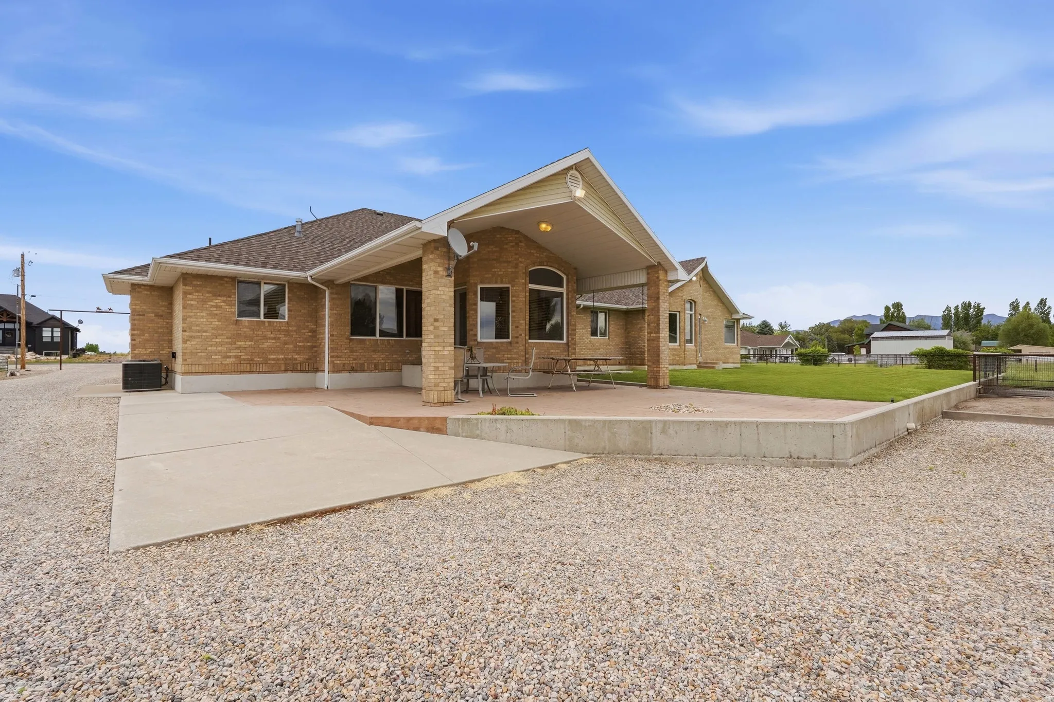 Rear exterior featuring a covered patio, expansive concrete slab, and a gravel surface