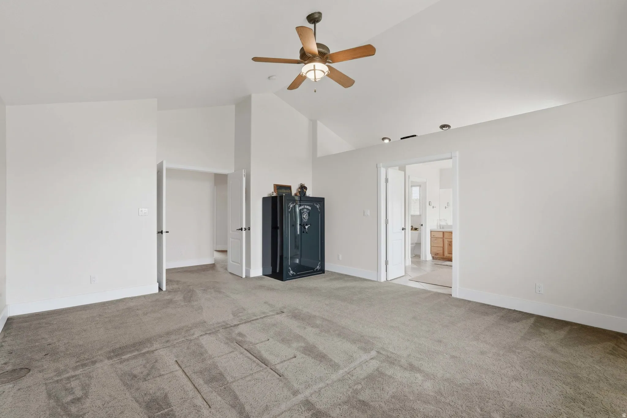 Spacious room featuring vaulted ceilings, neutral carpet flooring, and a ceiling fan with integrated lighting