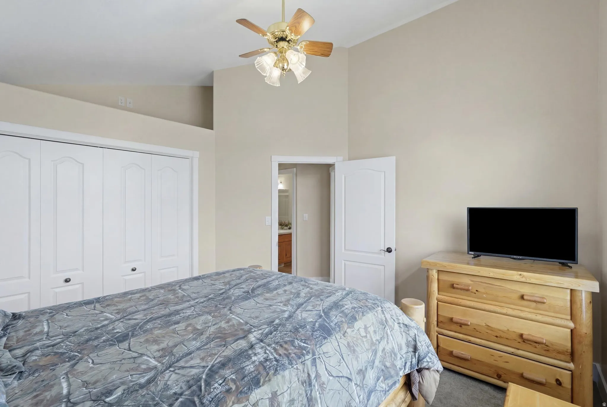 Vaulted ceiling with a ceiling fan light fixture, two-panel bifold closet doors, and neutral wall paint
